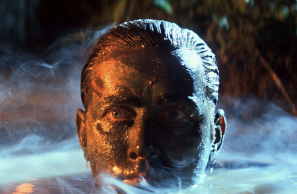 A man rises from a bog, his face covered in mud and substances this editor cannot determine.